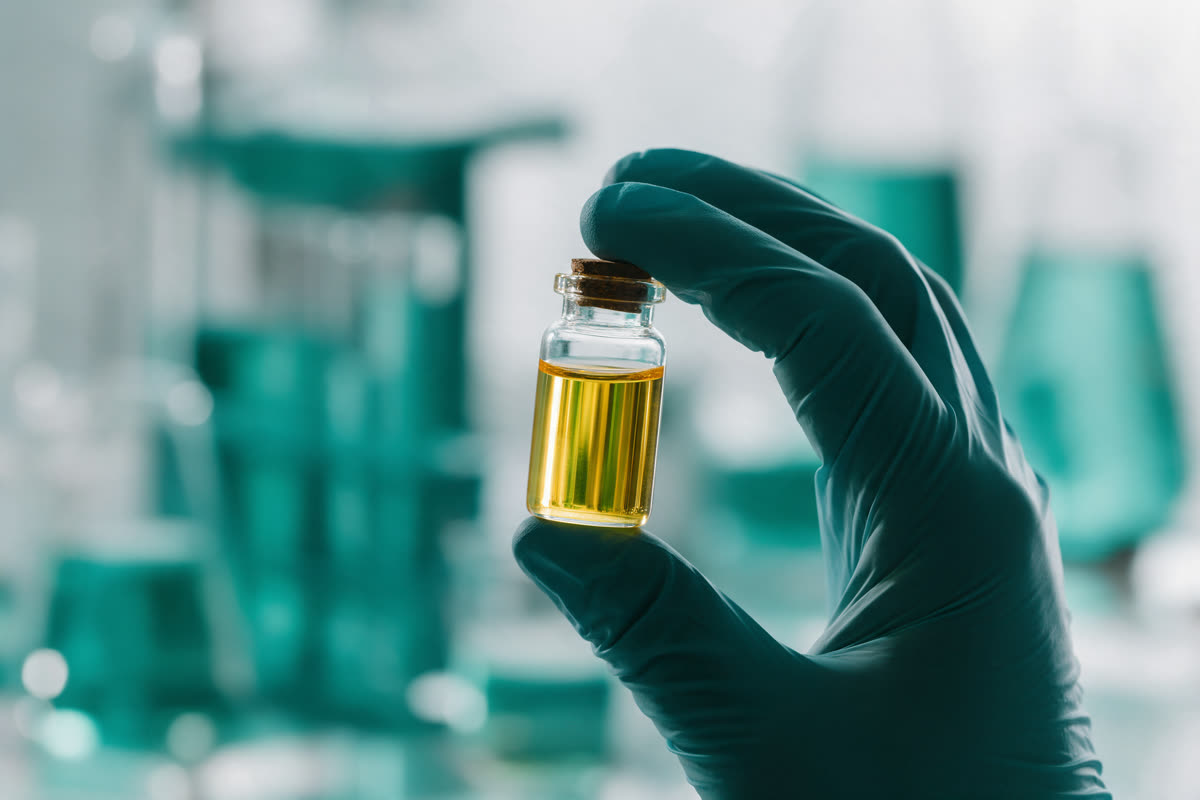 Gloved hand holding a vial of clear golden oil up to the light